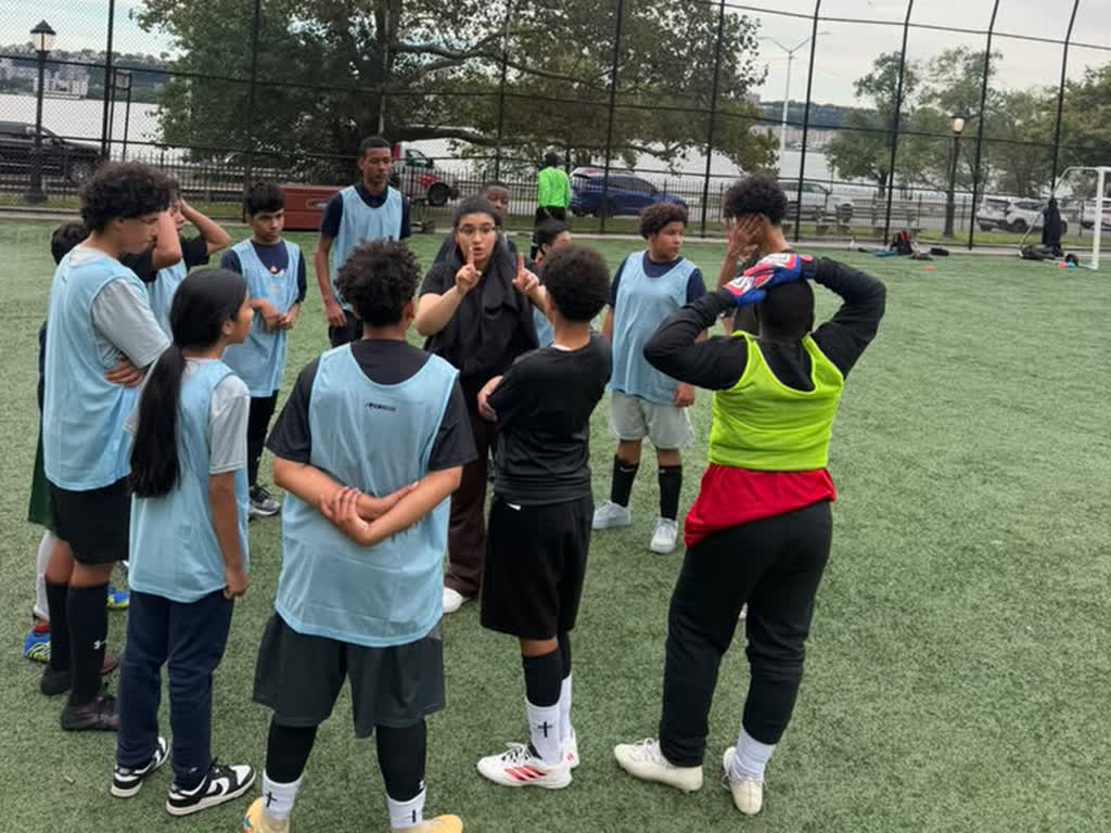 A coach talking with a huddle of MSC Hawks soccer players on the turf field